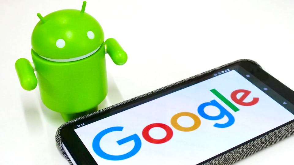 An Android phone with Google displayed on it with the Android mascot standing over it. 